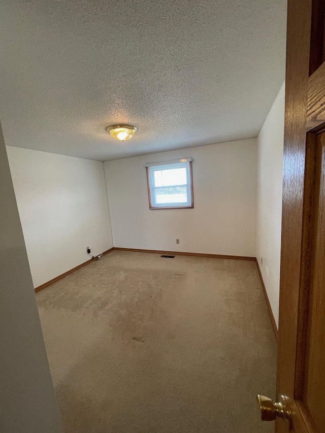 spare room with a textured ceiling, light colored carpet, visible vents, and baseboards