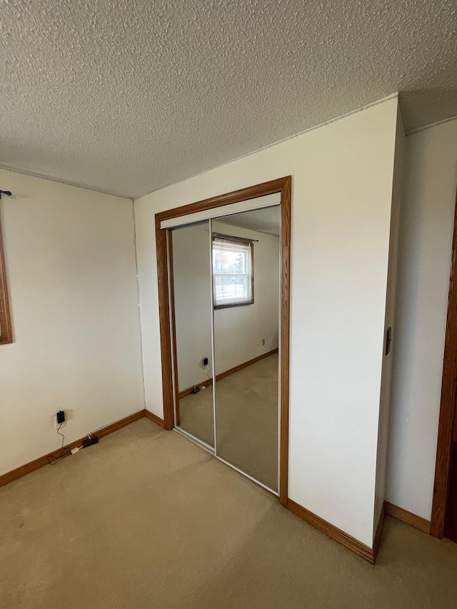 unfurnished bedroom featuring a textured ceiling, baseboards, a closet, and light carpet