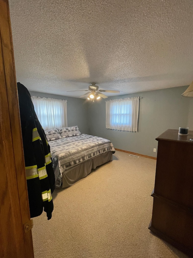 carpeted bedroom with a textured ceiling, a ceiling fan, visible vents, and baseboards