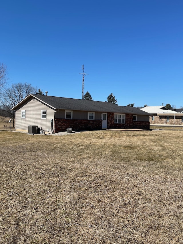 rear view of property featuring central AC unit and a lawn