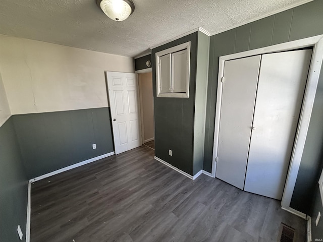 unfurnished bedroom with visible vents, a textured ceiling, a closet, and dark wood-style flooring