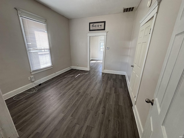 unfurnished room with baseboards, visible vents, and dark wood-style flooring