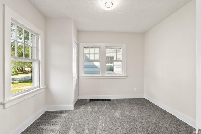 spare room with visible vents, dark carpet, a textured ceiling, and baseboards