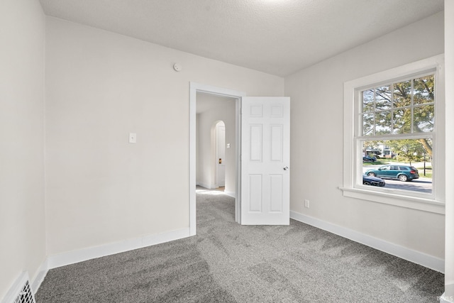 carpeted empty room with visible vents, baseboards, and arched walkways