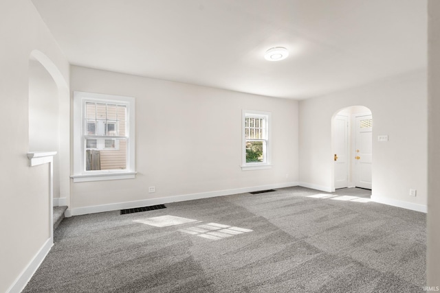 carpeted spare room featuring arched walkways, visible vents, and baseboards