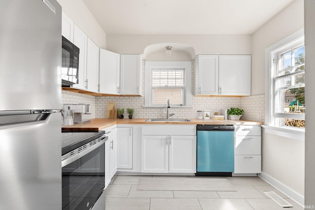 kitchen featuring visible vents, butcher block countertops, a sink, appliances with stainless steel finishes, and backsplash