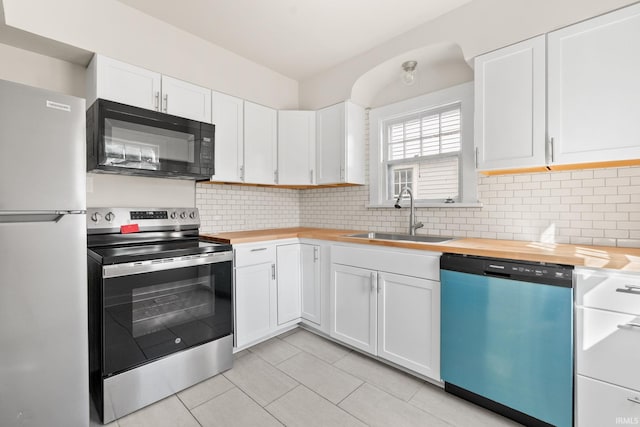 kitchen featuring butcher block countertops, decorative backsplash, appliances with stainless steel finishes, white cabinetry, and a sink