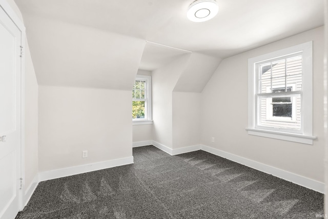 additional living space featuring lofted ceiling, baseboards, and dark colored carpet