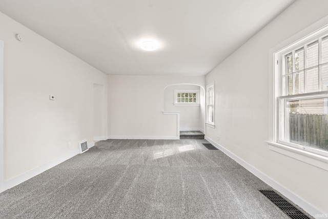 carpeted empty room featuring visible vents, baseboards, and arched walkways