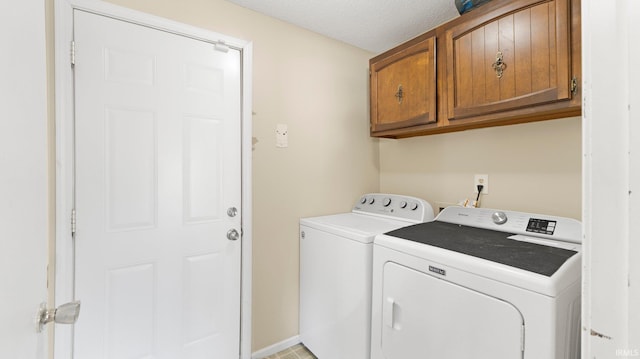 clothes washing area with cabinet space, washer and dryer, a textured ceiling, and baseboards