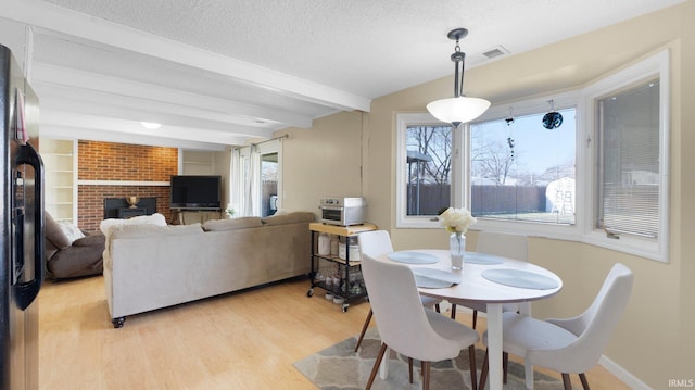 dining space with beam ceiling, light wood-style flooring, a textured ceiling, baseboards, and a brick fireplace