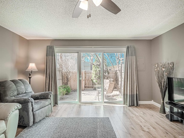 living area featuring a ceiling fan, wood finished floors, baseboards, and a textured ceiling