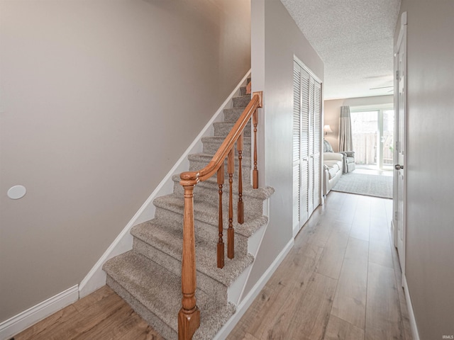 stairs featuring wood finished floors, baseboards, and a textured ceiling