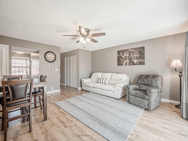 living room featuring a textured ceiling, light wood-type flooring, baseboards, and a ceiling fan