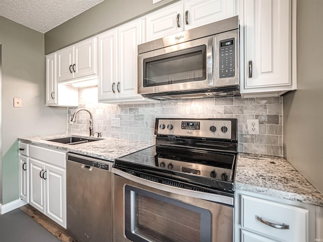 kitchen with light stone counters, white cabinets, appliances with stainless steel finishes, and a sink