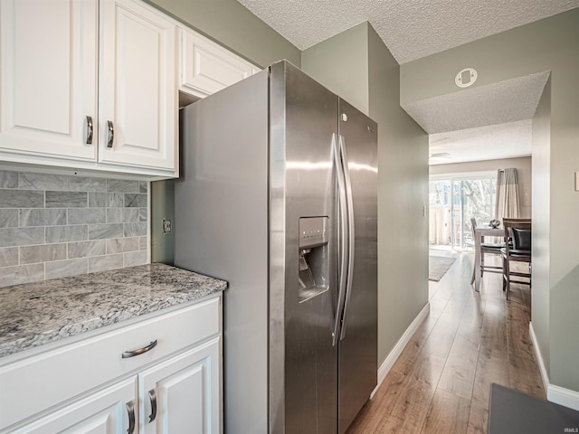 kitchen featuring light wood-type flooring, decorative backsplash, stainless steel refrigerator with ice dispenser, and white cabinetry