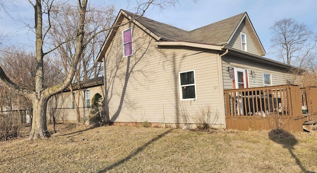 view of side of home with a wooden deck, a lawn, and fence