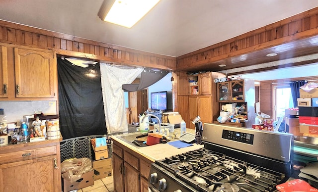 kitchen featuring stainless steel range with gas stovetop, wood walls, light countertops, light tile patterned floors, and a sink