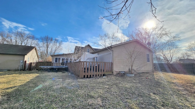 rear view of house with a yard, a wooden deck, a trampoline, and fence