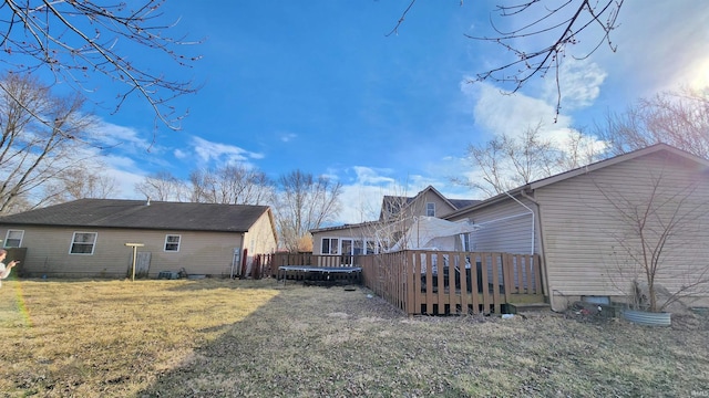 rear view of house featuring a wooden deck, a trampoline, and a lawn