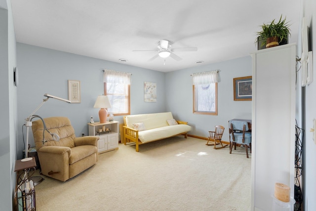 living area featuring a ceiling fan, light colored carpet, baseboards, and a wealth of natural light