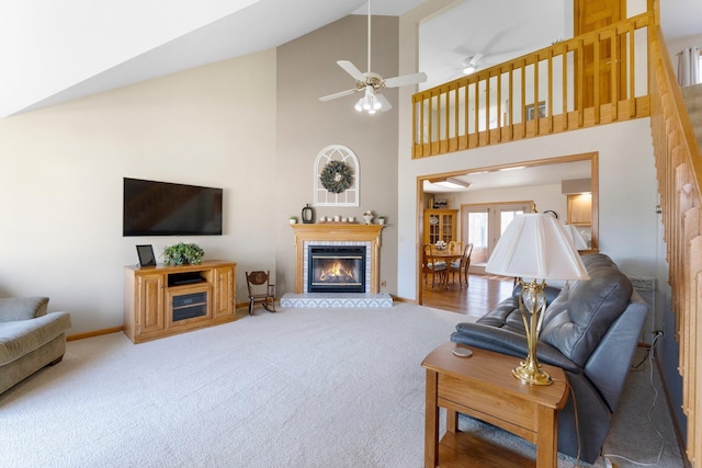 carpeted living room with ceiling fan, baseboards, high vaulted ceiling, and a glass covered fireplace