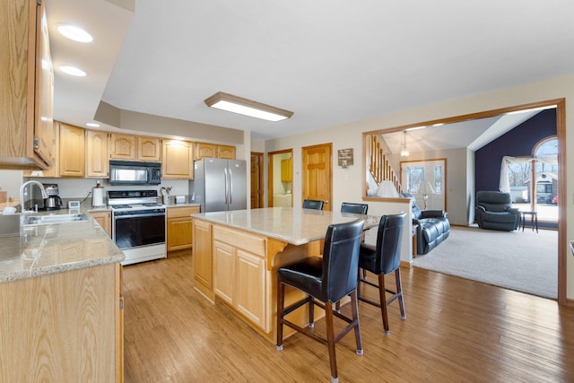 kitchen with black microwave, white range with electric cooktop, light brown cabinetry, freestanding refrigerator, and a sink