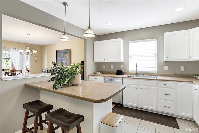 kitchen featuring a sink, hanging light fixtures, white cabinets, dishwasher, and a kitchen bar