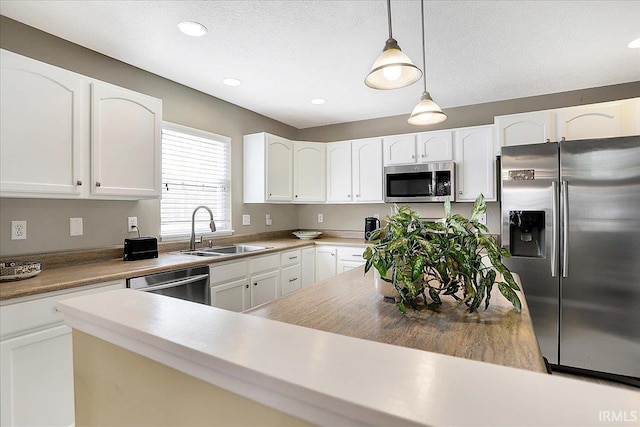 kitchen with a sink, appliances with stainless steel finishes, pendant lighting, and white cabinetry