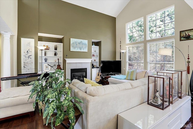 living area featuring a tiled fireplace, decorative columns, dark wood-style flooring, and high vaulted ceiling