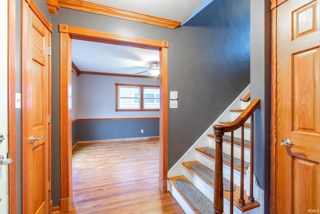 stairs with a ceiling fan, wood finished floors, baseboards, and ornamental molding