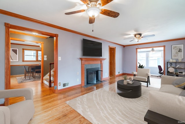 living area featuring wood finished floors, visible vents, baseboards, a fireplace, and crown molding