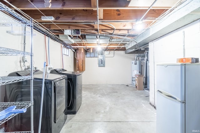 unfinished below grade area featuring gas water heater, washing machine and clothes dryer, electric panel, and freestanding refrigerator