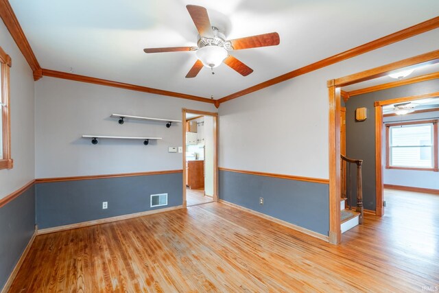 unfurnished room featuring a ceiling fan, wood finished floors, visible vents, and ornamental molding