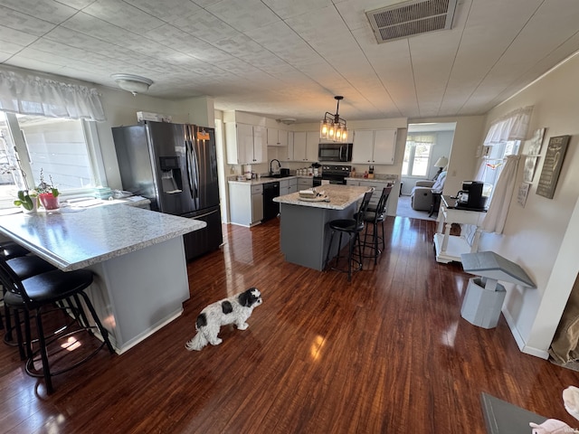 kitchen with visible vents, a center island, a kitchen breakfast bar, black appliances, and a sink