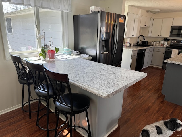 kitchen with a sink, dark wood-type flooring, black appliances, and light countertops