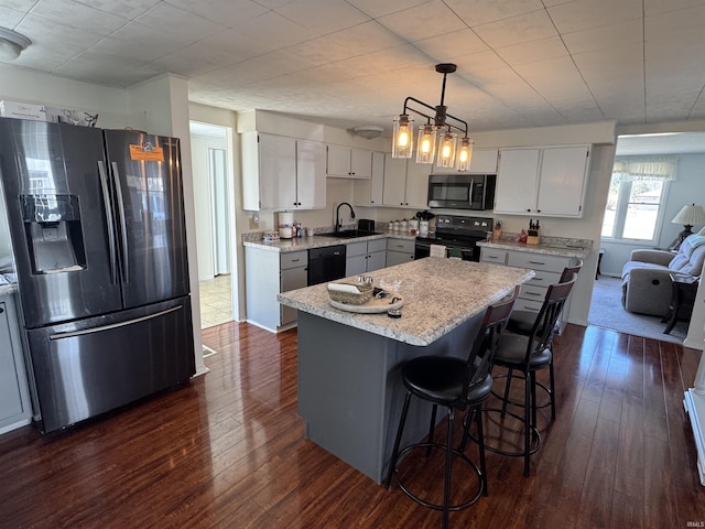 kitchen with dark wood-type flooring, black appliances, a breakfast bar, a sink, and a kitchen island