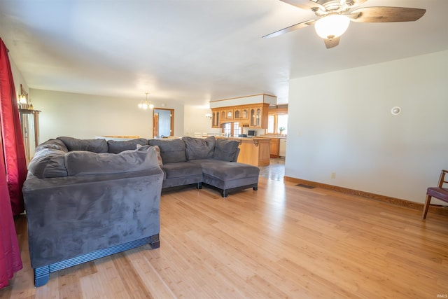 living area featuring visible vents, light wood-style flooring, ceiling fan with notable chandelier, and baseboards