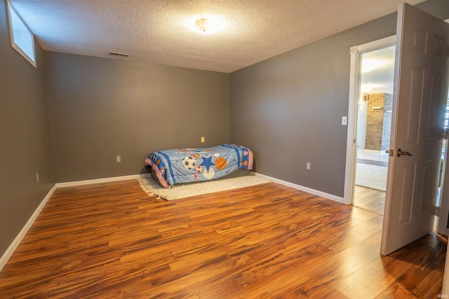 unfurnished bedroom with visible vents, baseboards, a textured ceiling, and wood finished floors