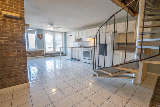 kitchen with a textured ceiling, white appliances, brick wall, white cabinets, and decorative backsplash