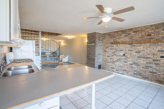 kitchen featuring brick wall, white cabinets, a textured ceiling, a ceiling fan, and a sink