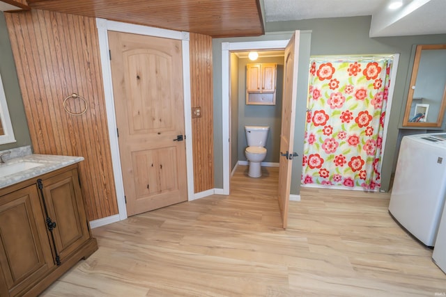 full bathroom featuring toilet, a shower with shower curtain, washer / dryer, wood finished floors, and vanity