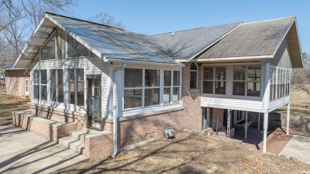 rear view of property featuring a patio area, brick siding, a sunroom, and a shingled roof