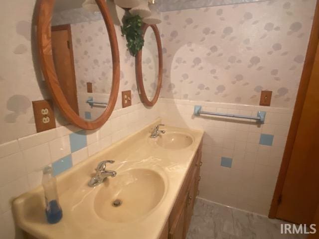 bathroom with a sink, a wainscoted wall, and wallpapered walls