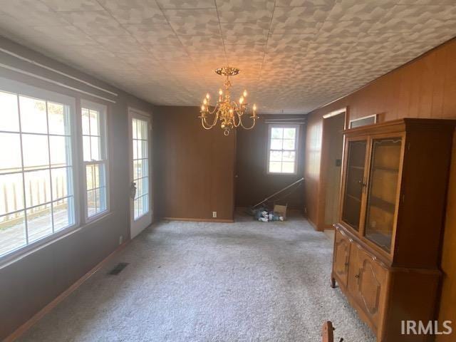 unfurnished dining area featuring light carpet, visible vents, and a chandelier