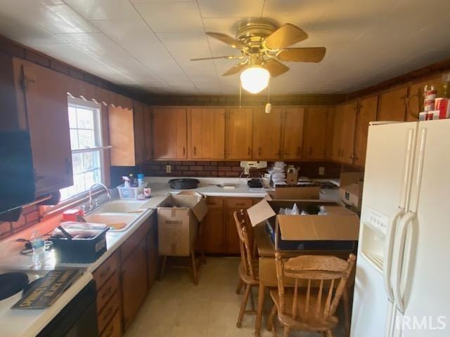 kitchen featuring light countertops, brown cabinets, white refrigerator with ice dispenser, a ceiling fan, and a sink