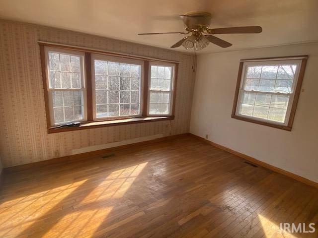 spare room featuring wallpapered walls, a ceiling fan, baseboards, and hardwood / wood-style flooring