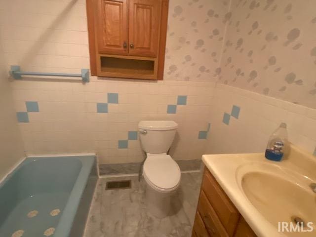 bathroom with wallpapered walls, toilet, a wainscoted wall, and a washtub