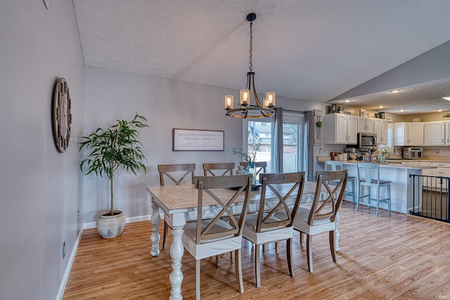 dining space with baseboards, light wood-style flooring, vaulted ceiling, a textured ceiling, and a notable chandelier