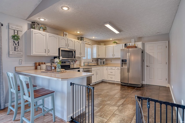 kitchen featuring a kitchen bar, appliances with stainless steel finishes, a peninsula, white cabinets, and a sink